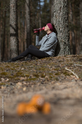 The girl rests after playing sports. Dumbels close-up and a bottle of water in hand. Exercise charging in nature. photo