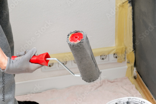 Girl holds a roller in hand close-up. Girl repaints the wall in gray. Repair in the room. DIY repair.