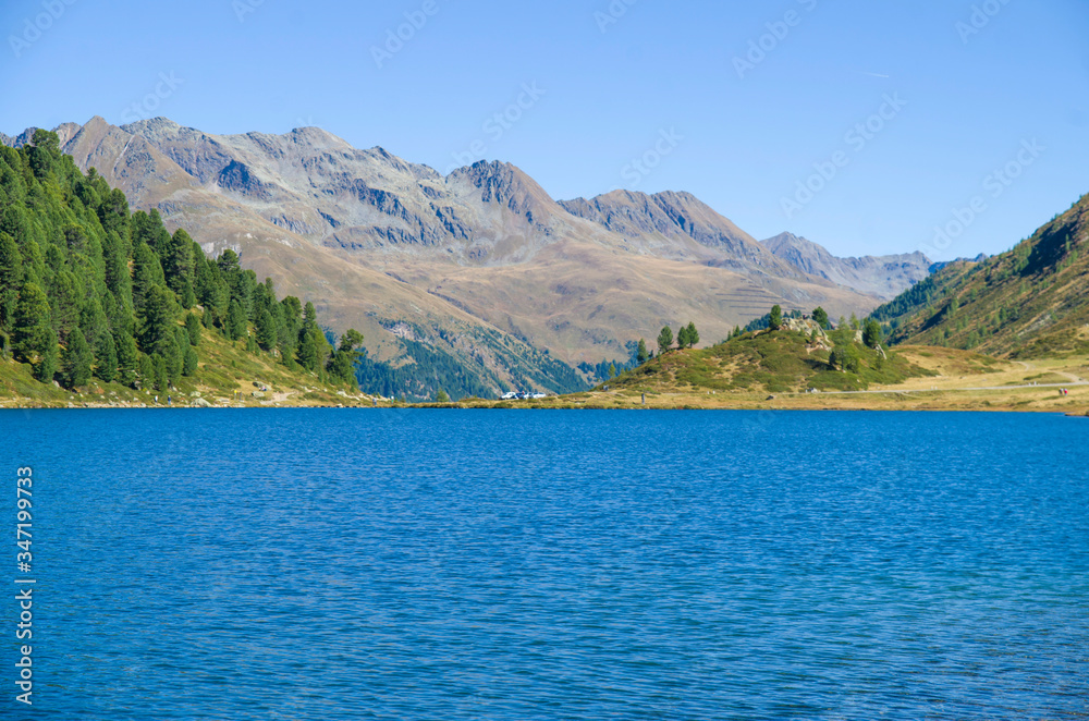 bright blue mountain lake under blue sky with woods, stones and snow