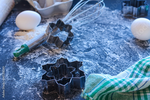 Baking utensils and ingredients are spread out on the dark surface.