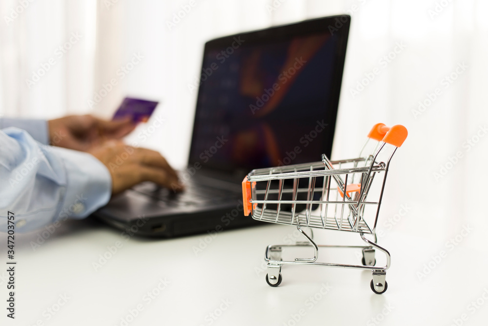 Empty supermarket shopping cart with man using laptop and holding credit card background, Online shopping concept