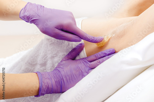Master beautician removes hair from female underarm with sugar paste  white color. Sugaring beauty concept