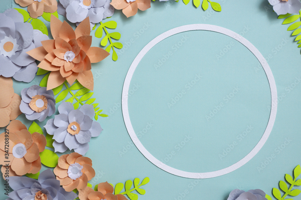 Flat lay of vintage round card frame, color paper flowers design on blue background. Top view, copy space, floral art