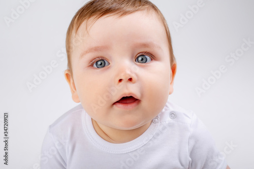 portrait of a cute baby boy with blue eyes in a white bodysuit against a white background  space for text