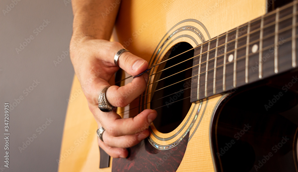 Fototapeta premium A hand with vintage rings playing a guitar. Close-up view. Selective focus. Grain.