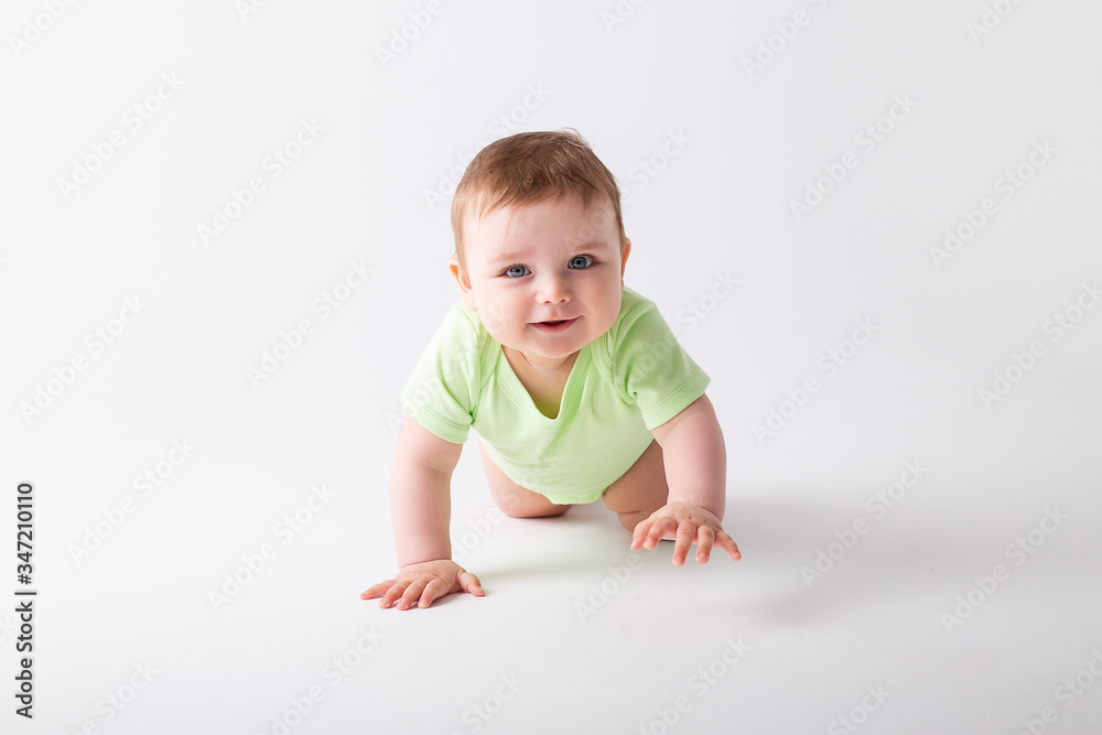 Cute toddler in green bodysuit sits with green apples on white background Cute toddler in green bodysuit sits with green apples on white background