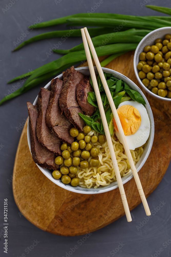 Asian traditional soup in a bowl on a wooden stand. Beef pho bo with eggs and green peas. Top view.