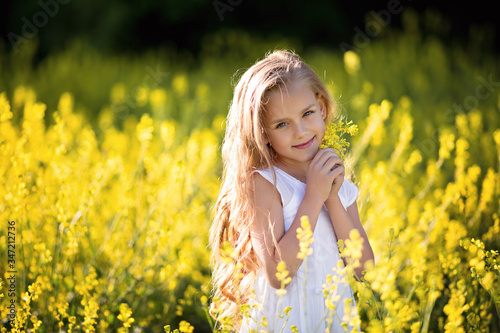 Portrait of a cute happy little girl 5-7 years old in nature  in the summer in a rape field.