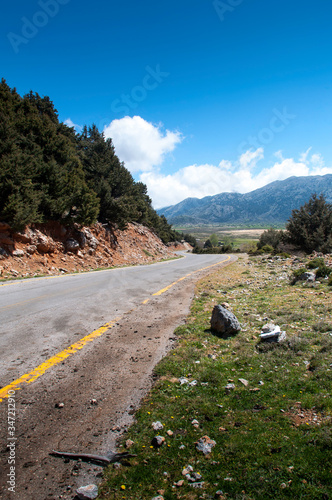 A lonely deserted road leads through the mountains or highlands on the Greek island of Crete. The road loses itself on the horizon. White clouds can be seen in the sky. photo