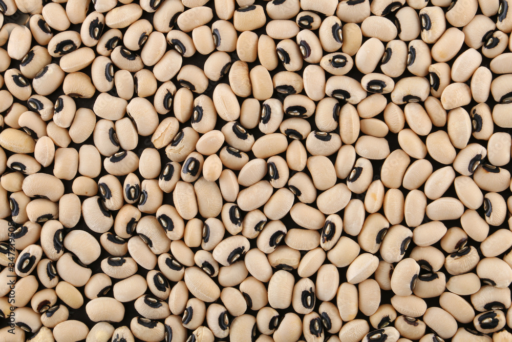 Background texture of dried black-eyed peas or beans, Vigna unguiculata, or cowpea, with a spoonful in a wooden spoon, grown as a staple nutritional crop, as animal fodder and to enrich soil Background texture of dried black-eyed peas or beans, Vigna unguiculata, or cowpea, with a spoonful in a wooden spoon, grown as a staple nutritional crop, as animal fodder and to enrich soil