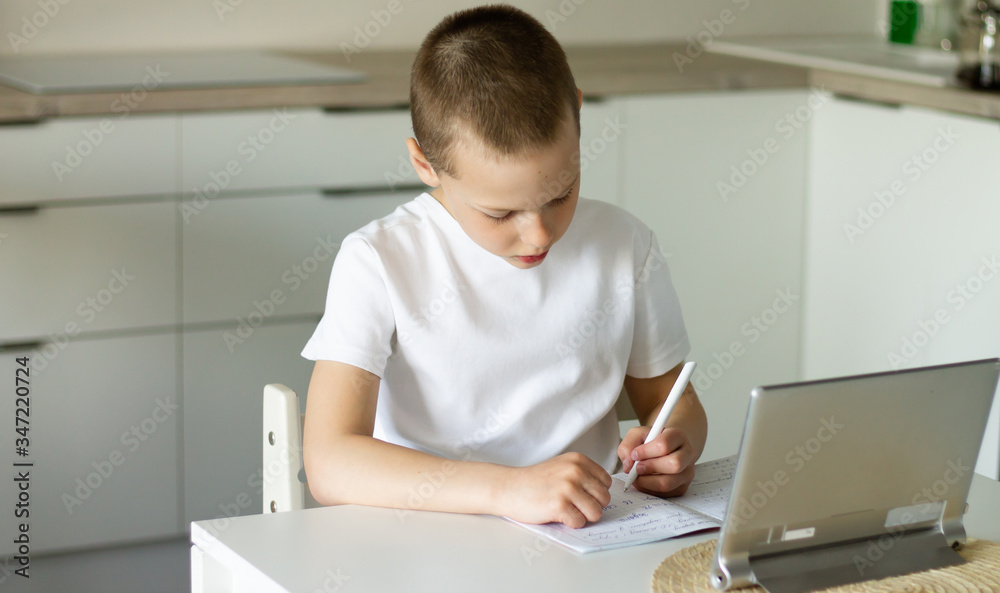 Boy 6-10 completes school lessons and homework online in the kitchen, looking at the tablet computer. The concept of distance education. Stay at home. Boy 6-10 completes school lessons and homework online in the kitchen, looking at the tablet computer. The concept of distance education. Stay at home.