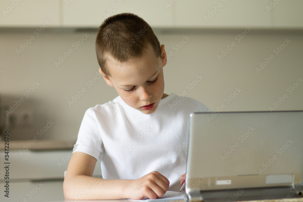 Boy 6-10 completes school lessons and homework online in the kitchen, looking at the tablet computer. The concept of distance education. Stay at home. Boy 6-10 completes school lessons and homework online in the kitchen, looking at the tablet computer. The concept of distance education. Stay at home.