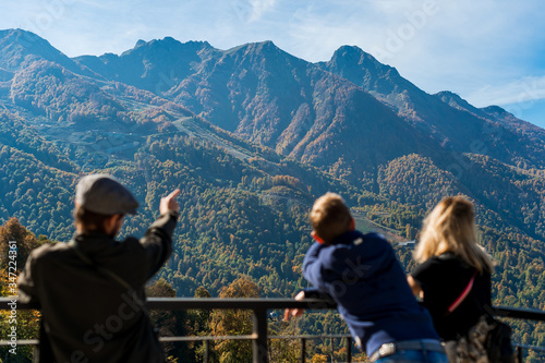 Sochi, Rosa hutor. Company of friends admires the mountain landscape on a sunny automn day. Young man showes beautiful landscape to his friends. © Anton