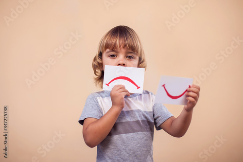A portrait of kid boy holding cards with mood expression. Childhood and emotion concept