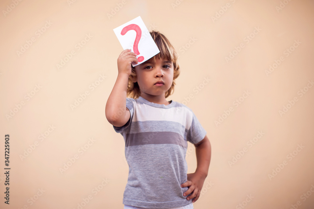 A portrait of kid boy holding cards with question mark. Childhood and education concept A portrait of kid boy holding cards with question mark. Childhood and education concept