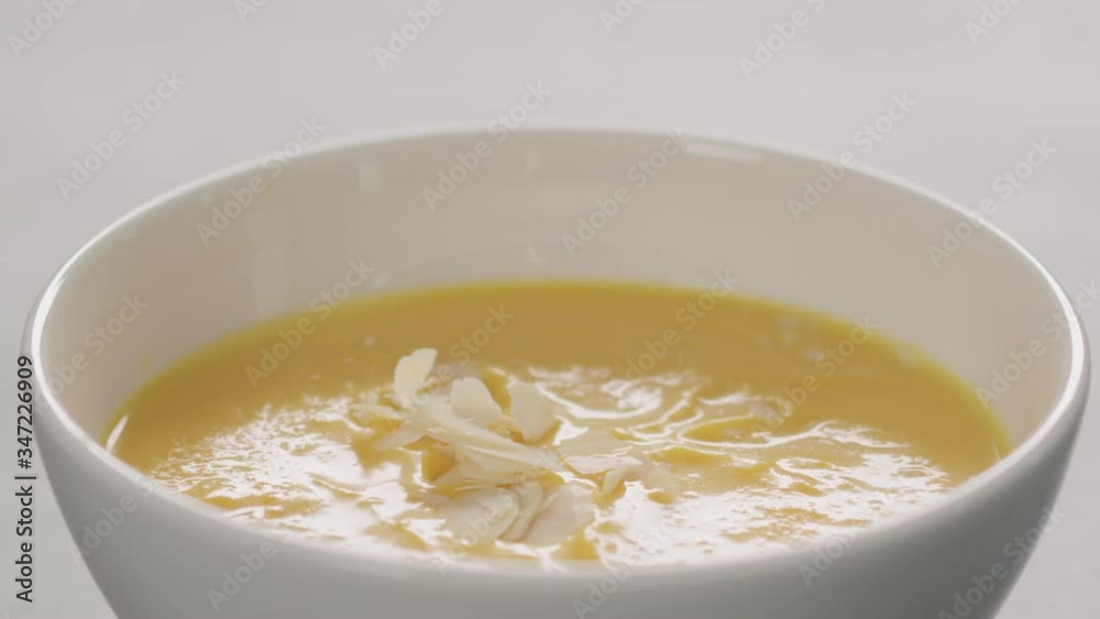 Slow motion almond flakes fall in pumpkin cream soup in white bowl closeup Slow motion almond flakes fall in pumpkin cream soup in white bowl closeup