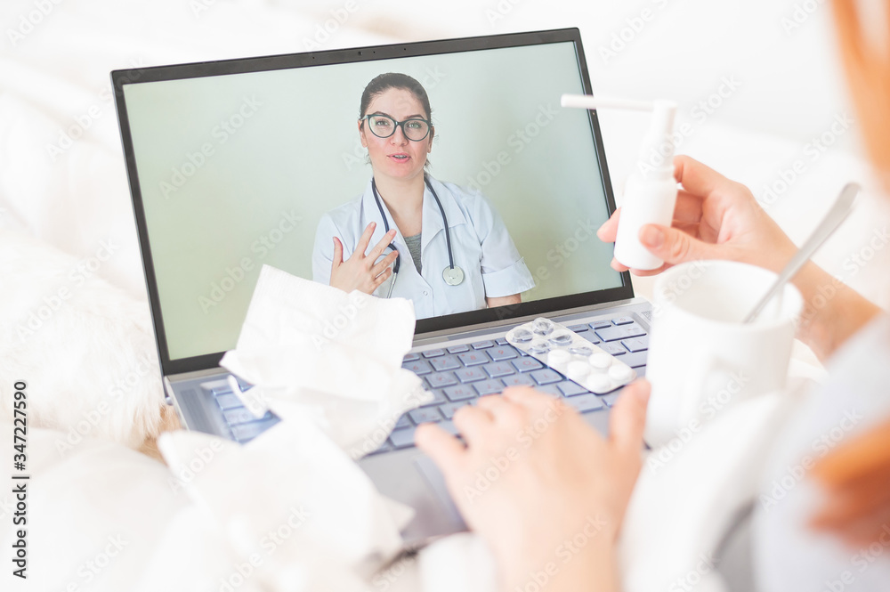 Telemedicine concept. Close-up of a doctor on a smartphone display during an online medical consultation with a patient. Wooden tray with medicines and a thermometer on the patient's bed. Telemedicine concept. Close-up of a doctor on a smartphone display during an online medical consultation with a patient. Wooden tray with medicines and a thermometer on the patient's bed.