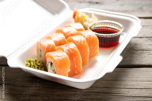 Box with rolls Philadelphia soy sauce and wasabi on a wooden background. Japanese kitchen. Food delivery.