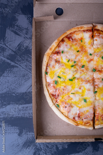Pizza with cheese in the cardboard box on the grey table. Top view. Copy space. Food delivery concept