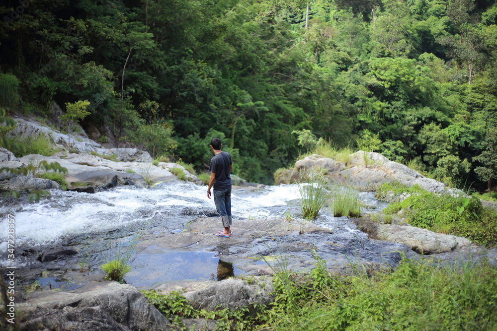 Man standing at Khlong Nam Lai waterfall in Klong Lan national park, Kamphaeng Phet, Thailand Man standing at Khlong Nam Lai waterfall in Klong Lan national park, Kamphaeng Phet, Thailand