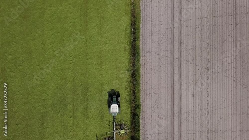 Traktor mit Heuwender bringt nach Mahd der Wiese Grasschnitt für Grassilage in Reihe, Landwirtschaft aus der Vogelperspektive