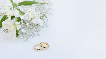 Flowers and two golden wedding rings on white background.