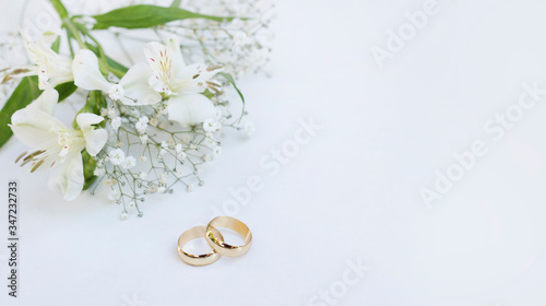 Flowers and two golden wedding rings on white background.