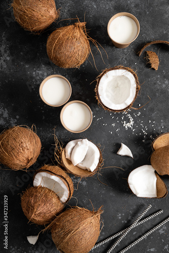 Coconut milk, whole and cracked coconuts on black background, top view