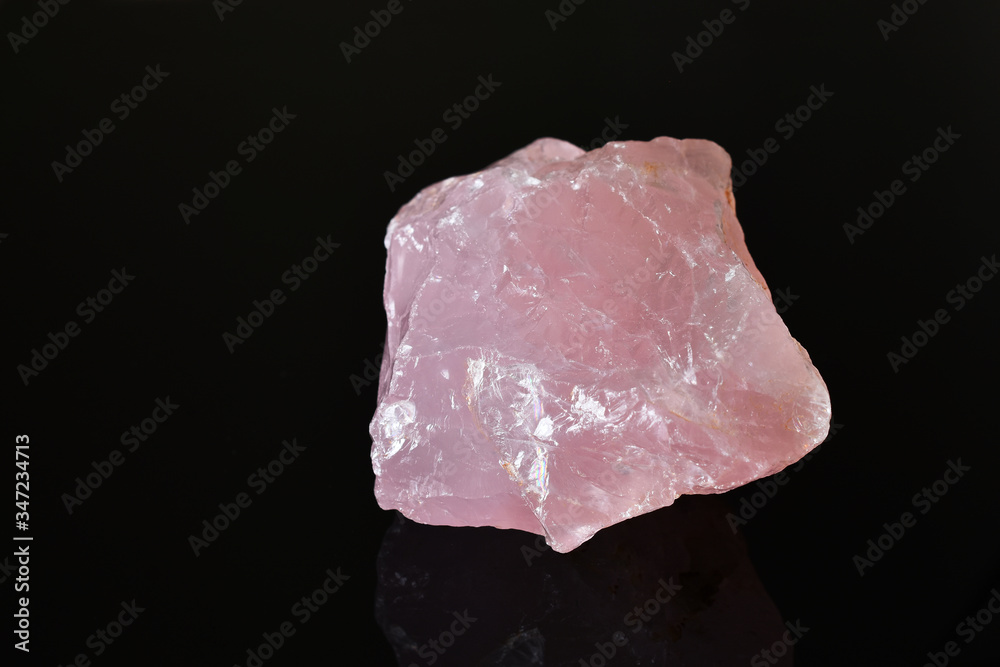 An image of an uncut rose quartz crystal on a black background. 