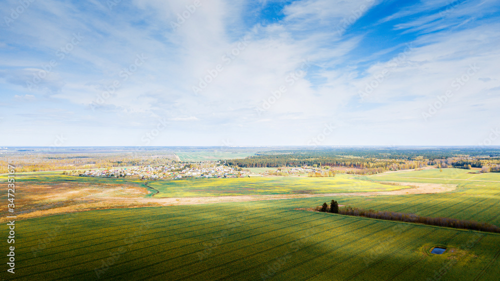 Aerial view over the rural landscape. Small village, trees, fields, classic blue sky and nature background.