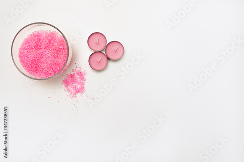 Three light pink candles stand next to the bowl. Nearby, bath salt is poured. Items for spa treatments. Gentle colors. Horizontal photo. Space for text.