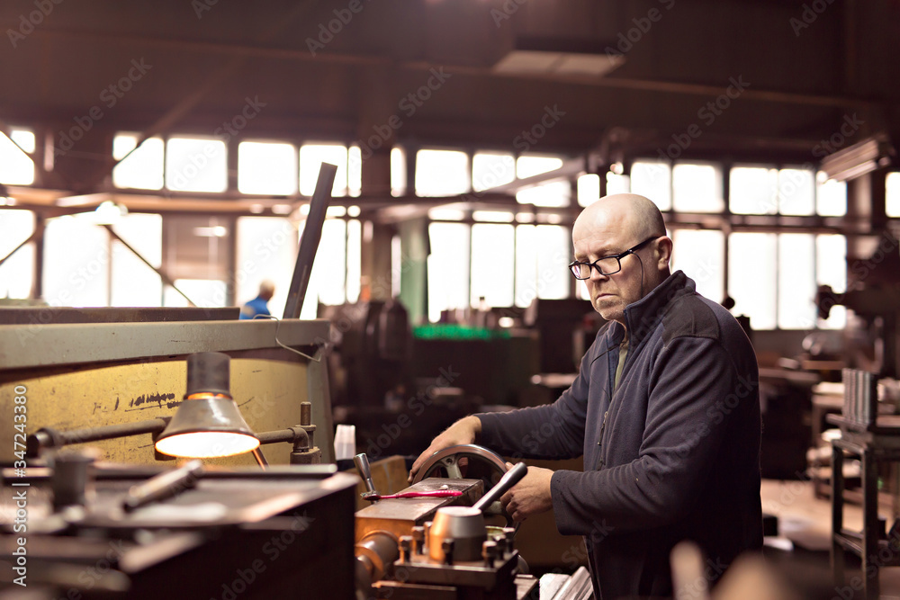 A man 50-60 le works at the machine at the factory. Man with glasses. Hard work. A man 50-60 le works at the machine at the factory. Man with glasses. Hard work.
