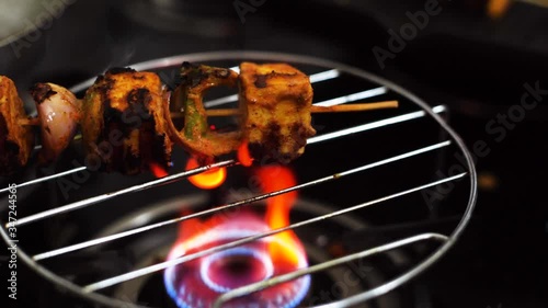 hand turning a skewer of paneer shimla mircha pepper spice onion tomatoes and more over a grill on a gas stove to make tandoori grilled paneer cottage cheese photo