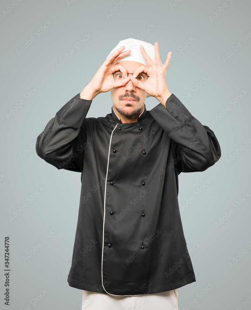 Amazed young chef using his hands like a binoculars Amazed young chef using his hands like a binoculars