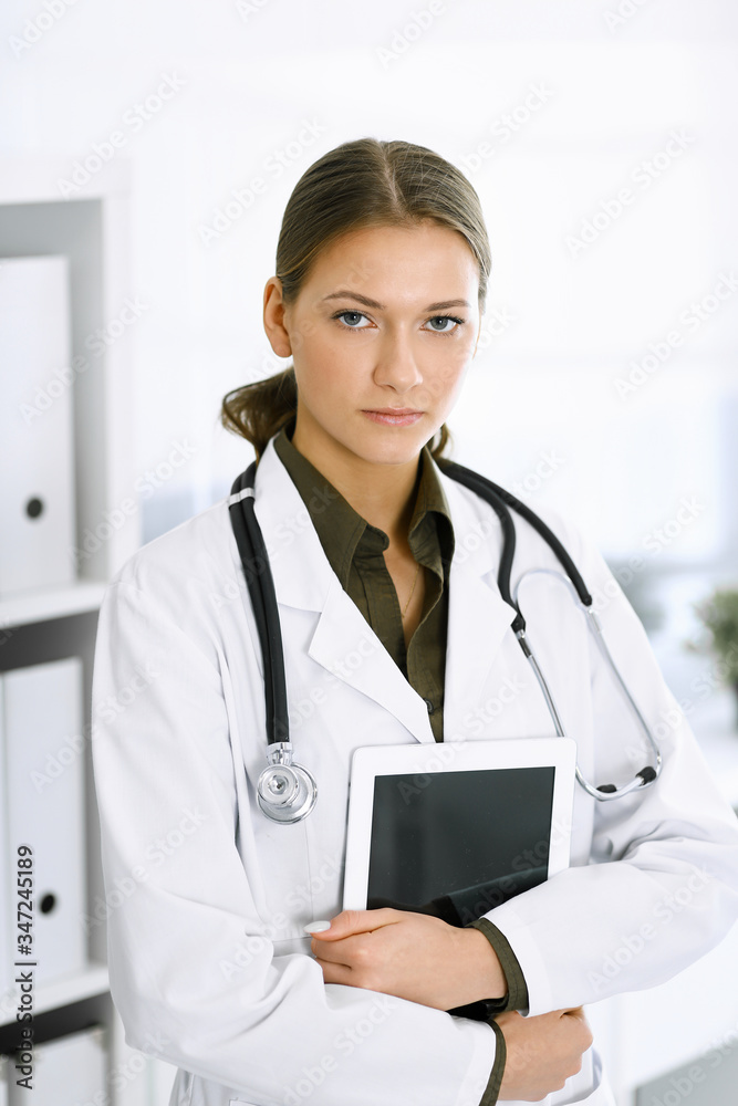 Woman-doctor standing and looking at camera. Perfect medical service in clinic. Medicine and healthcare Woman-doctor standing and looking at camera. Perfect medical service in clinic. Medicine and healthcare