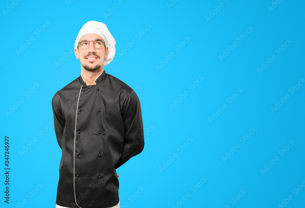Happy young chef looking against background Happy young chef looking against background