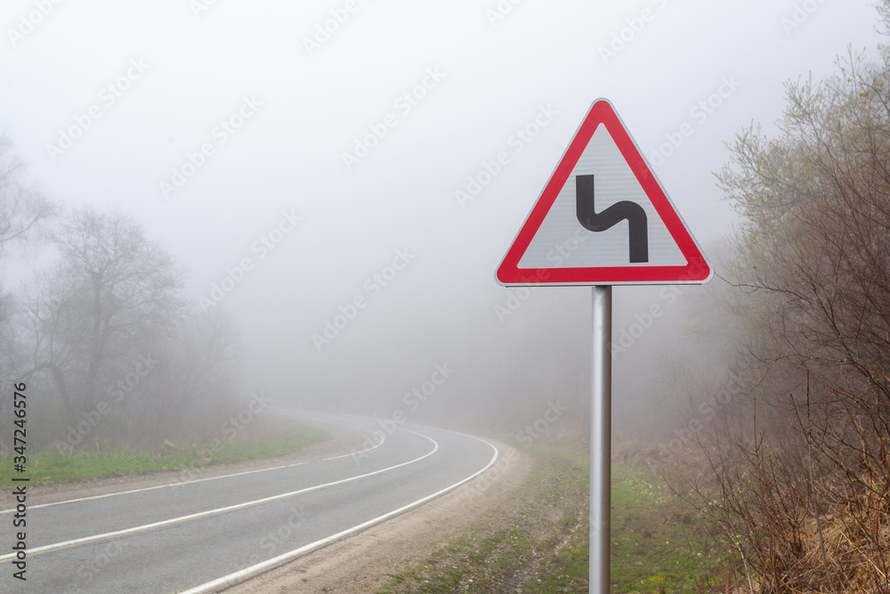 Road sign mountain serpentine. Mountain road in the fog Road sign mountain serpentine. Mountain road in the fog