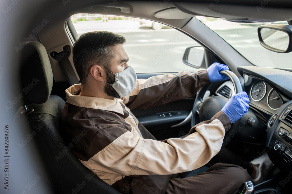 Young man in workwear, mask and gloves holding steer while driving to clients