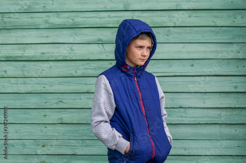 Funny handsome teenage boy is posing for camera. Outdoor portrait of a teenage boy on green background. Expressive boy with a hood on his head photo