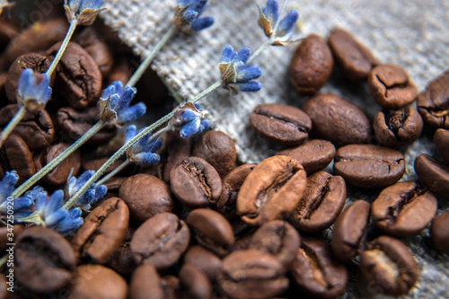 Coffee beans close-up, spilled on the table. Coffee beans on a background of burlap, decorated with branches of dried lavender. Beautifully blurred background. Macro photo.