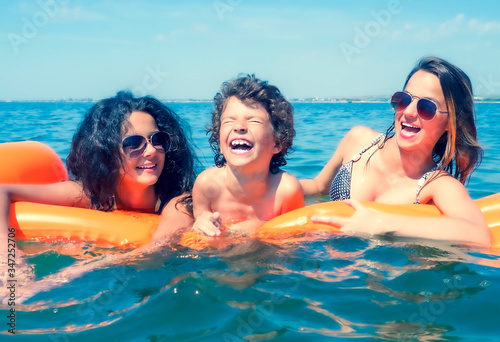 Happy young family positive mom and two little daughters swim on a yellow air mattress in the sea on a sunny summer day during vacation. Vacation concept abroad. Copyspace © kravik93