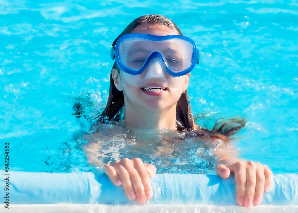 Naklejka premium A cute happy young girl child relaxing on the side of a swimming pool wearing golubots goggles.