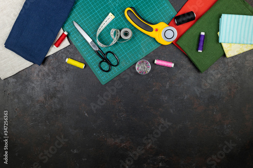 quilting, embroidery and sewing tools on the dark background. patchwork knife, scissors, lined cutting mat, self-locking, threads, measuring tape, floss, hoop . copy space. flat lay