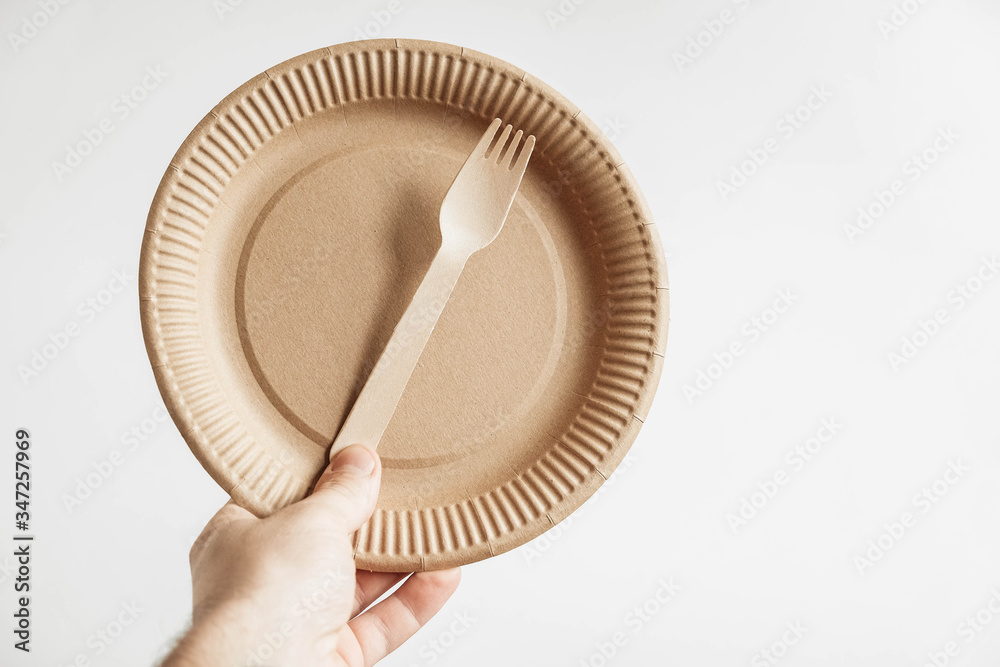 Men hand holding a wooden fork and disposable paper plate on white background. Copy, empty space for text Men hand holding a wooden fork and disposable paper plate on white background. Copy, empty space for text