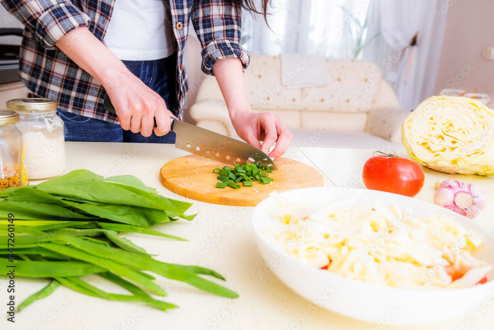 Woman slices green onions in a vegetable salad. A woman is preparing a salad of fresh vegetables in the kitchen.