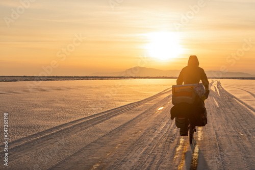 Bicyclist on the sunset with Olkhon Island on background. Baikal Lake, Russia, february 2020