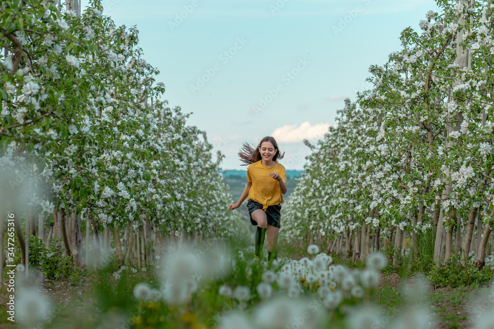 Happy brunette girl in yellow shirt running along blooming trees in the apple garden Happy brunette girl in yellow shirt running along blooming trees in the apple garden