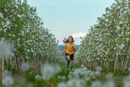 Happy brunette girl in yellow shirt running along blooming trees in the apple garden