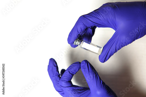 The doctor's hands in blue medical rubber gloves hold a vial with the inscription COVID-19. Medical concept, a vial of coronavirus, a cure and a vaccine, the fight against the epidemic. White 