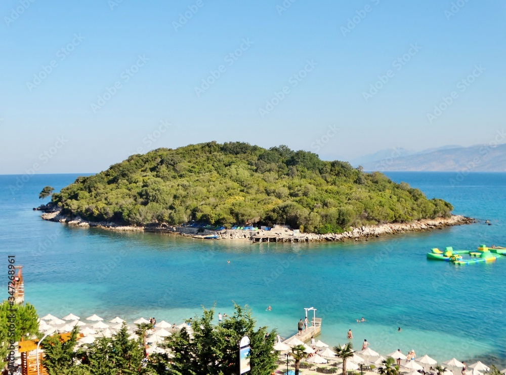 Fotografía de las preciosas islas con abundante bosque rodeadas por el agua transparente de color turquesa del Mar Jónico, con pequeñas embarcaciones, un día de verano en la playa de Ksamil, Albania